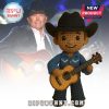Crochet cowboy doll with black hat and guitar in front of concert background.