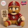 Crochet 49ers football doll holding sign and ball on brown background.