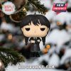 Wednesday Addams ornament with arms crossed on snowy Christmas tree.