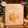 A soft pink advent calendar box with golden embossed text and cartoon bunnies sitting on a moon, surrounded by Christmas decor and cozy holiday ambiance!