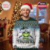 Man wearing a Grinch and Green Bay Packers ugly Christmas sweater stands in a cozy room with Christmas decor, showcasing the festive holiday design!