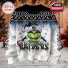Close-up view of the front design on a white and black Christmas sweater featuring the Grinch with folded hands, icy Raiders text, and festive snowflake and light string details.