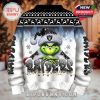 Rear view of a Raiders Christmas sweater showcasing the same Grinch illustration, logo on the Santa hat, and decorative holiday elements against a snowy gradient background.