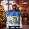A man in a Santa hat models a Grinch-themed Rams Christmas sweater in a cozy living room with Christmas lights, a decorated tree, and a glowing fireplace!