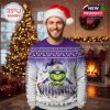 A smiling man in a purple and white holiday sweater with a Vikings-themed Grinch design, standing in a festive living room decorated for Christmas!