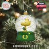 A detailed snow globe ornament with Woodstock from Peanuts, holding a flag inside a glittery dome on a green Oregon Ducks base!