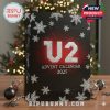 U2 holiday calendar styled with bold contrast colors, snow details, and collector-worthy signatures, placed beside ornaments on a wooden surface!