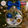 A glass Christmas ornament containing miniatures of a baseball jersey a cap a trophy and equipment set against a background of festive lights!