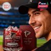 A fan grinning with excitement as he shows off a glass of red drink in a specially designed Atlanta Falcons anniversary glass, with the box in the background.