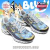 A pair of light blue sneakers with Bluey character designs and paw prints shown against a cartoon backdrop. The shoes are detailed with white laces, yellow accents, and a white sole!