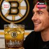 A close-up of a fan admiring his limited-edition Bruins whiskey glass with the team logo, city etching, and shimmering golden drink, backed by team colors!