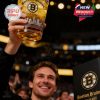 The crowd roars as a man celebrates Boston Bruins history by toasting with a sleek whiskey glass engraved with skyline art and gold accents, spotlighted in the arena!