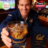 A man at a bar smiling and offering a Cal 143rd anniversary whiskey glass with the boxed set nearby!