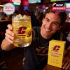 A college fan holds up a Chippewas whiskey glass beside a yellow box creating a friendly bar atmosphere!