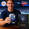 A man in a team shirt poses with a collectible CF Montréal whiskey glass featuring the club logo and gold cityscape design, with a dark display box beside it!