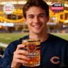 A close-up of a happy fan showing off the Chicago Bears 2025 glass filled with golden drink and bold logo, just outside the stadium!