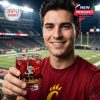 A supporter stands on the field holding a red Bearcats whiskey glass with gold details and team mascot visible!