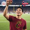 A fan proudly holds up a Cincinnati Bearcats collector whiskey glass with red tones and gold artwork against a stadium background!