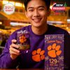 Young Clemson fan in purple holding branded whiskey glass with ice, beside commemorative gift box at brightly lit stadium!