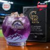 A Colorado Rockies 33rd anniversary whiskey glass in purple with ice sits next to a black and gold gift box in a baseball stadium setting!