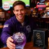 A man in a bar smiles while presenting the Colorado Rockies 33rd anniversary purple whiskey glass with the commemorative box resting on the table next to him!