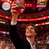 Wearing a blazer and white shirt, the fan raises the glass in celebration at a hockey arena, capturing the emotion of the Red Wings’ 100-year legacy!