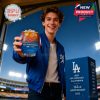 A young fan in Dodgers attire lifts a limited edition glass with ice, showcasing it under the glowing lights of a stadium while standing next to a branded anniversary box!
