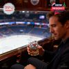 Stylish man with whiskey glass in hand, seated at a luxury arena box looking out over a hockey rink, immersed in the atmosphere of the game.