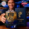 Smiling man holding FIU whiskey glass in bar with branded box behind.