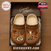 Tan-colored Crocs with George Strait branding, featuring country-themed designs like guitars and a skull.