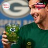 Man in Green Bay Packers apparel holding and admiring the commemorative glass with green drink in front of a blue background featuring the team logo!