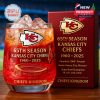 Kansas City Chiefs whiskey glass with anniversary branding and detailed etchings of the stadium, set against a blurred background of a stadium.
