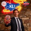 Man in suit holding KU whiskey glass in front of neon Jayhawk sign.