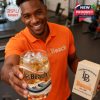 A man in a casual orange polo shows off a detailed Long Beach State whisky glass and gift box with wave artwork and university logo!