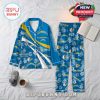 Blue Chargers pajamas with floral prints and team logos, placed on a bed with cozy props like a coffee cup, slippers, and an open book!
