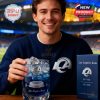 Person holding a Los Angeles Rams whiskey glass, filled with blue liquid and ice, with the team’s logo and details clearly visible in the background of a football stadium.