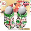A pair of white Christmas clogs decorated with colorful Zootopia characters, candy, holiday icons, and a large green ribbon in the center. The strap is green with “Your Name” in black, and the shoes say “Merry Christmas” near the toe!