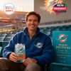 Whiskey glass with Miami Dolphins 1966 anniversary design held by smiling man in Dolphins fleece at stadium.!