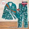 Aqua green Miami Dolphins pajamas with white floral overlays and custom name placement, laid flat on a wood-textured surface!