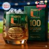 100th Anniversary Miami Hurricanes glass with team logo, gold stadium artwork, and decorative swirls, displayed beside matching gift box on wooden surface!