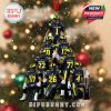 Christmas ornament of Michigan players in navy uniforms with maize accents, posed as a team pyramid under snowfall, ready to hang with red ribbon and trophy base!