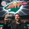 A man celebrates the team in style by holding up the green whiskey glass beneath the glowing Minnesota Wild logo!