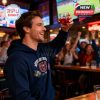 A spirited sports fan dressed in team apparel toasts with the Missouri State Bears limited-edition glass during an energetic game night at the bar!