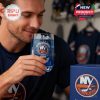 A man in team apparel holds and drinks from a special NY Islanders glass, featuring anniversary artwork and filled with icy blue liquid, with team jerseys in the background!