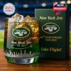 A clear whisky glass featuring the New York Jets logo anniversary text city skyline artwork and a green presentation box on a wooden surface!