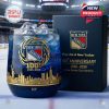 A commemorative New York Rangers whisky glass with rich blue color gold emblem and skyline design shown with collector packaging on an ice rink!