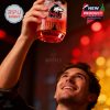 A man holds the red NIU whiskey glass overhead, smiling under red ambient lighting at a festive indoor event!