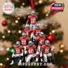 Football-themed ornament with Ohio State players posed in a pyramid shape, wearing red and silver uniforms. A red ribbon loop hangs the ornament on a festive Christmas tree, with a trophy at the base!