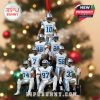 Holiday ornament showing nine Ole Miss football players in white uniforms forming a pyramid pose. The base features a trophy and a red hanging ribbon is attached at the top. Background includes Christmas lights and festive tree décor!