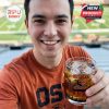 A person holding the Oregon State Beavers whiskey glass filled with ice, in front of a football field, representing team pride.